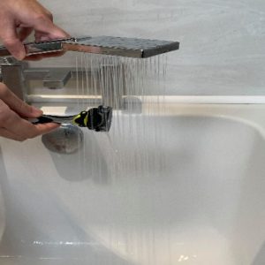 Person rinsing the razor with the shower head after each motion to remove the hair