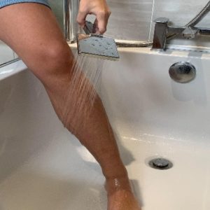 Person rinsing their leg with the shower head while standing in the bath