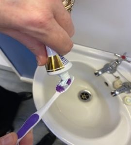 Person squeezing a pea sized amount of toothpaste onto a toothbrush