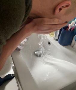 Person standing over a sink and rinsing their face