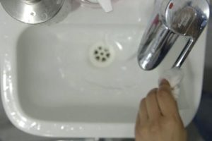 Person using the disposable towel to turn off the tap