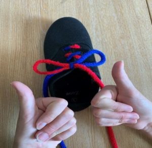 Person with their thumbs up having completed the task of tying their shoe laces