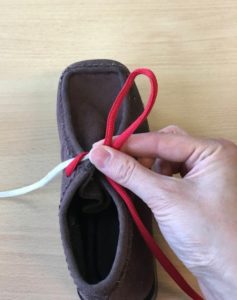Picture shows someone making a bunny loop with the red lace and securing it between their thumb and index finger