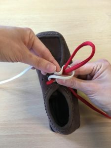 Picture shows someone pushing the back of the white lace (wrapped around the red loop (bunny ear) through the hole where their right thumb rests