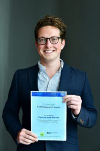 Bespectacled man in suit holding an awards certificate