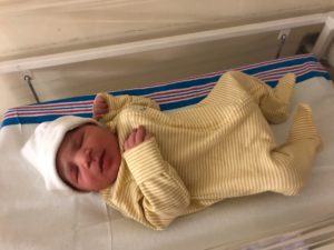 Baby Willow laying in her cot in a stripey yellow baby grow and white hat